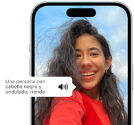 Un iPhone 15 muestra cómo la funcionalidad lee la descripción de una imagen: una persona con pelo negro ondulado sonriendo